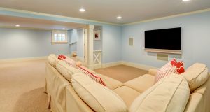 Spacious basement living room interior in pastel blue tones. Beige carpet floor and large corner sofa with TV.