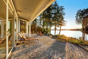 Large stone floor patio area of waterfront house with outdoor furniture beautiful water view at sunset.