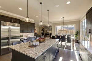 Modern gray kitchen features dark gray cabinetry paired with white quartz countertops and a glossy gray linear tile backsplash. Bar style kitchen island with granite counter.